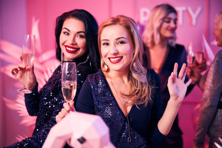 Two glamorous ladies with happy smiles on their faces and champagne flutes in their handsの写真素材