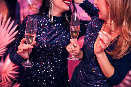 Cropped photo of a dark-haired and a blonde woman with glasses of sparkling wine smiling at each otherの写真素材