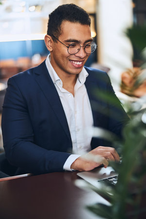 Waist-up portrait of a smiling pleased elegant cheerful young male telecommuter working on his laptopの写真素材
