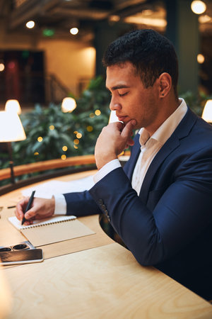 Side view of a Latin American man focused on writing his thoughts in the notebookの写真素材