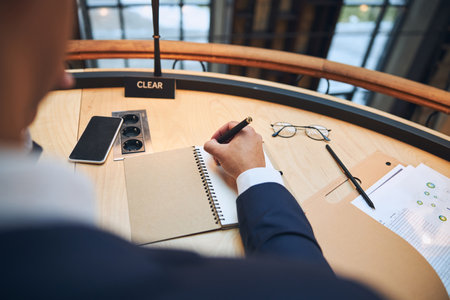 Cropped photo of a man in formal wear writing his thoughts with a ball-point pen in a spiral notebookの写真素材