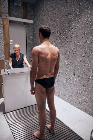 Young athletic man is coming for having Charcot douche during health procedures and recreation under female assistanceの写真素材