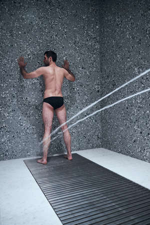 Slim male is standing under Charcot douche while being treated in modern medical spa centreの写真素材