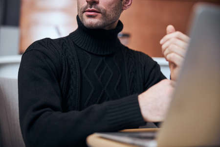Low angle cropped head of handsome stubbled guy sitting at table with laptop in hotel hall