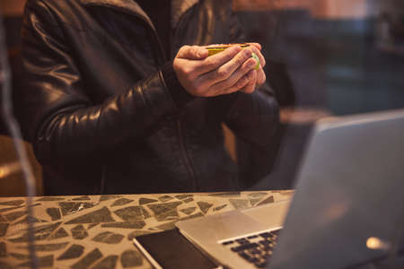 Cropped head low angle of man holding cup of tea while using laptop and smartphone in bar