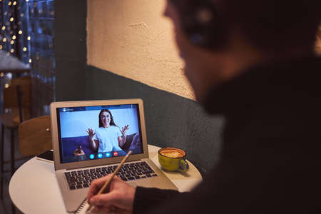 Top view of man in earphones listening to video on notebook and making notes in sketchbookの写真素材