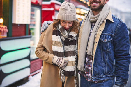 Cropped head of merry bearded guy embracing beloved girlfriend while they are walking in street