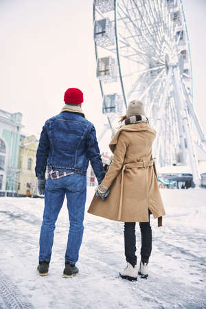 Happy woman and man are walking in city centre and holding each other hand on cold dayの写真素材