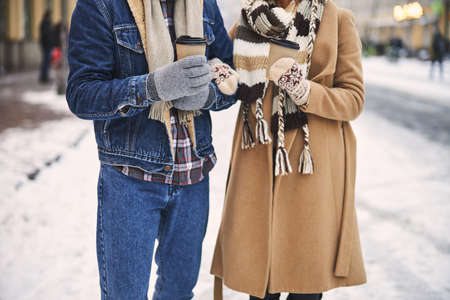 Cropped head of loving couple walking together in street in winter and carrying cups of hot drinks