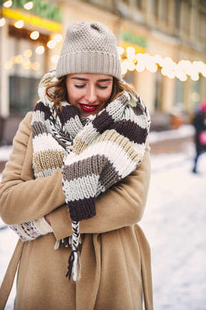 Cheerful pretty female is standing in lit urban street while walking on cold winter dayの写真素材