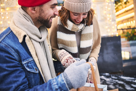 Jolly young man is walking in city with happy girlfriend while carrying paper bags with purchasesの写真素材