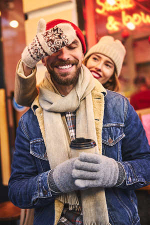 Happy young male and female are dating on cold day and buying hot drinks in street cafeの写真素材