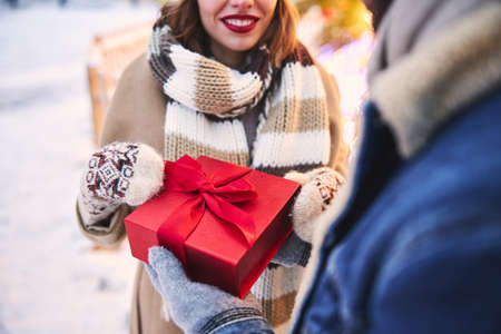 Cropped head of smiling pretty female holding box with present from man while walking together...
