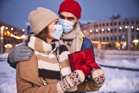Cheerful young man and woman in masks are celebrating Christmas in city centre with presentsの写真素材