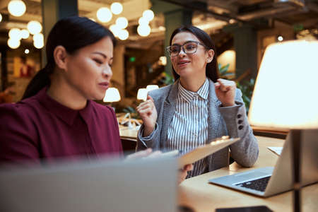 Cheerful female actively gesticulating while having pleasant conversation in modern business center