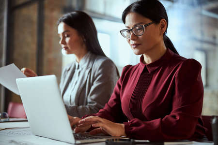 Attentive female person wearing glasses while sitting in front of her computerの写真素材