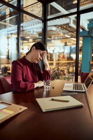 Negative delighted woman pressing her lips while suffering sharp headache at officeの写真素材