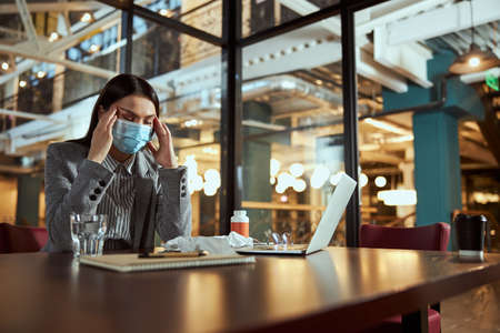 Young woman sitting at her workplace and massaging temples, keeping her eyes closedの写真素材