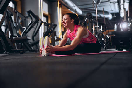Low angle of happy sporty female relaxing after hard workout on mat and bending in gymの写真素材