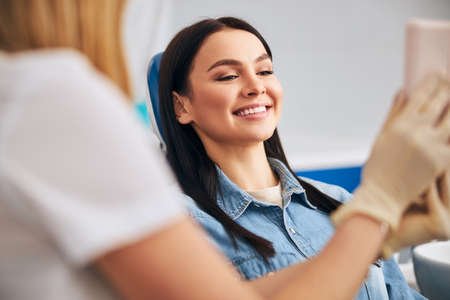 Young pretty female keeping smile on her face while consulting with her dentistの写真素材