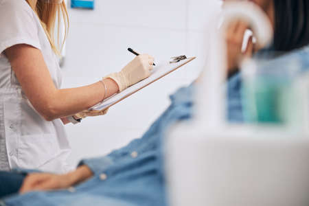 Professional stomatologist wearing uniform while working in modern clinic with her patientの写真素材