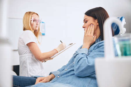 Concentrated medical worker sitting at her workplace while making notes during teeth checkupの写真素材