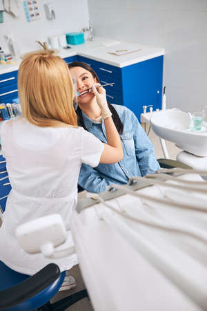 Positive delighted brunette sitting at dentistry chair while taking care of her teethの写真素材
