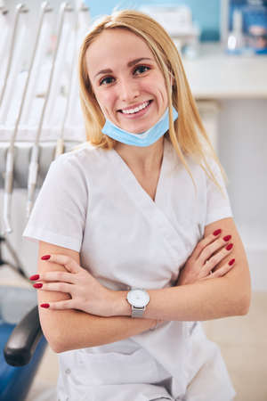 Sincere medical worker crossing arms on chest while sitting at her workplaceの写真素材