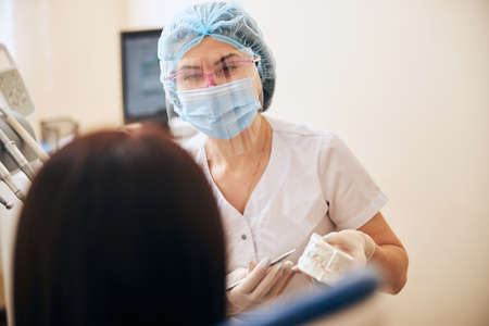 Professional dentist holding sterile instrument while giving consultation to her visitorの写真素材
