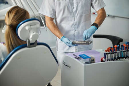 Male taking the edge of a stomatological tweezers and raising them with one hand from a small steel trayの写真素材