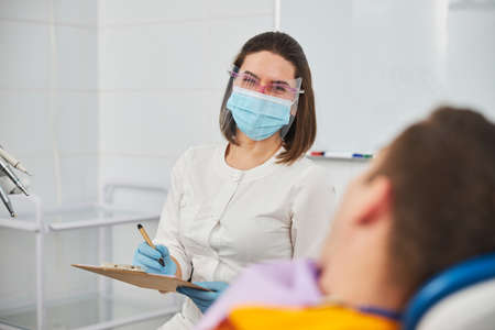 Female dentist laughing after hearing something funny from a man in operation chair while writing about his caseの写真素材