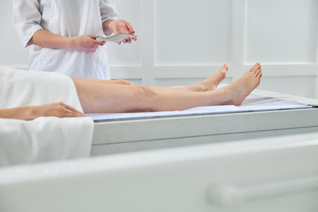 Close up of physical therapist holding medical massager while woman lying on massage tableの写真素材