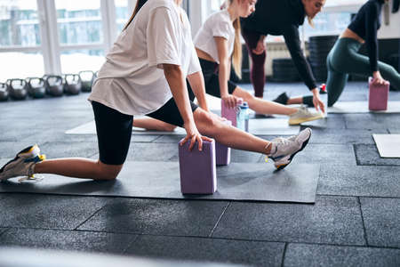 Cropped photo of slim women in sporty outfits stretching their legs with help of yoga blocksの写真素材