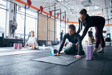 Professional yoga instructor assisting a young woman to get the position right at the gym