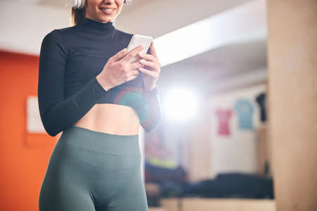 Cropped copy-space photo of slim young woman looking at her smartphone while standing at the gymの写真素材