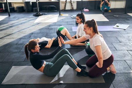 Ambitious young ladies doing set of abs exercises in pairs while working out at the gym