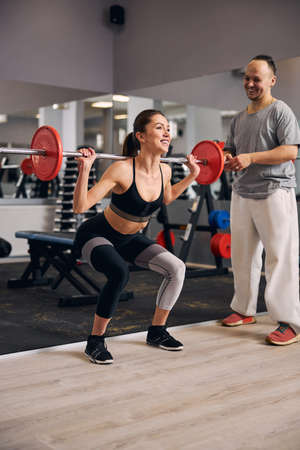Professional trainer supporting woman to lift weighsの写真素材