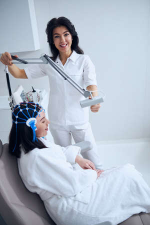 Friendly doctor in a lab coat carrying out the electroencephalography