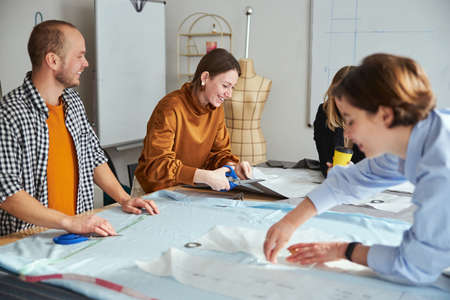 Cheerful couturiere laughing while cutting fabric materialの写真素材