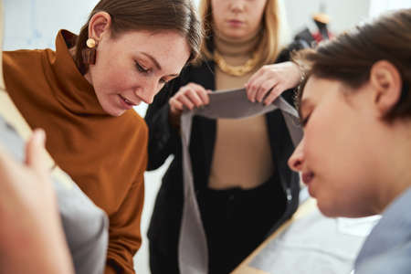 Couturiere bringing long grey fabric snip to two females