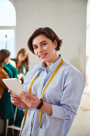 Couturiere wearing tape measure while keeping tablet