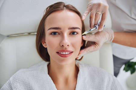 Happy elegant female lying on medicine chair and getting hyaluronic acid skincare in beauty clinicの写真素材