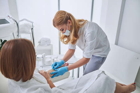 Beautiful elegant physician in white uniform during medical procedure in welness centerの写真素材