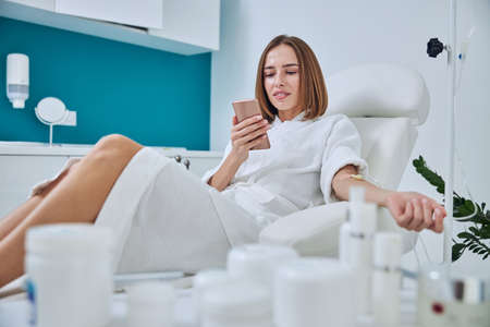 Happy smiling woman sitting in medicine armchair during medical procedure in beauty centerの写真素材
