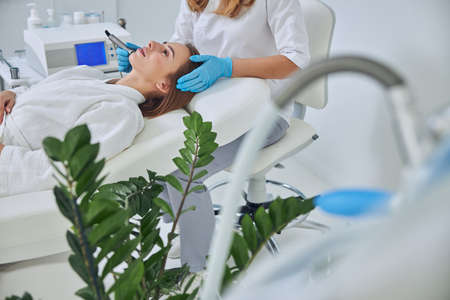 Charming Caucasian female in white bathrobe getting aesthetic cosmetology in beauty salon