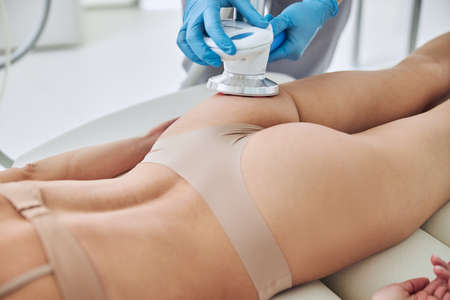 Unrecognized woman patient lying on medicine table while getting anti-fat treatment at beauty salonの写真素材