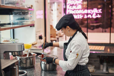 Concentrated female cook using wooden spatula for stirring