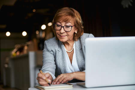 Beautiful female person making notes during online conferenceの写真素材