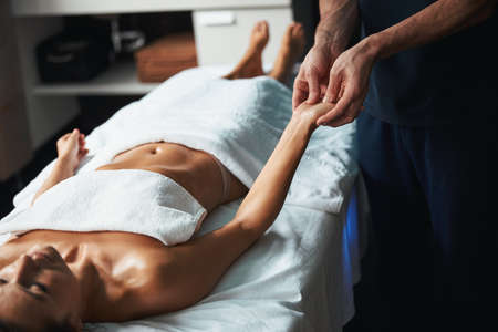 Beautiful charming woman under the towel lying on massage table receiving new massage technique in...