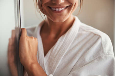 Happy cheerful pretty female in white bathrobe posing at the camera in spa salon